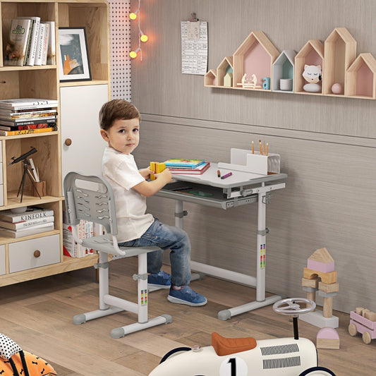 A young boy sits at the grey kids desk and chair set, doing homework in a bright room