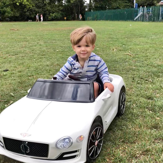 The ride-on car being driven by a young boy on a grassy park field