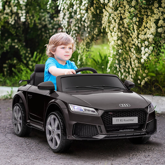 A young boy sitting in the black ride-on car outdoors in a garden setting