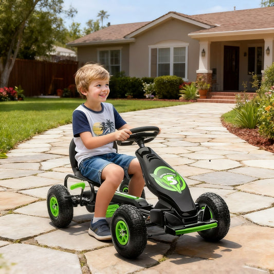 A young boy smiles as he pedals the green and black ride-on car along a paved driveway