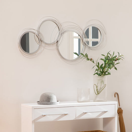 The decorative wall mirror hanging above a white console table with a grey hat and a vase of greenery