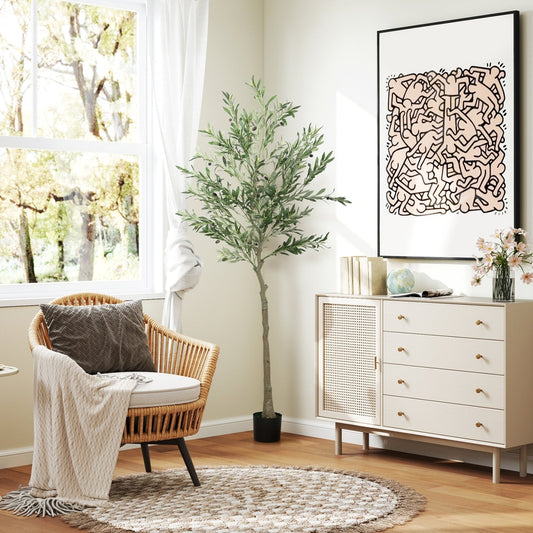 The artificial olive tree placed in a bright living room next to a rattan chair and a cabinet