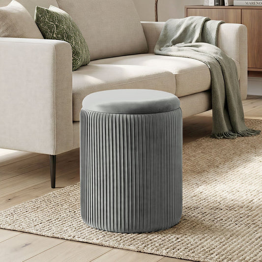 The grey velvet foot stool placed on a rug next to a sofa in a living room
