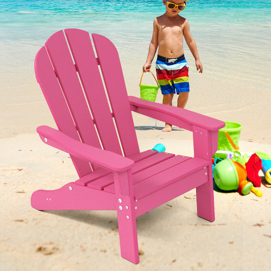A pink toddler lawn chair sits on a sandy beach with a child playing nearby