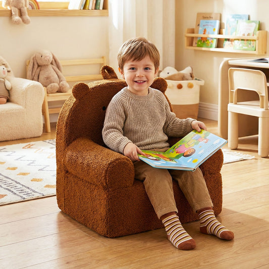 A young boy sits happily in the brown bear kids chair in a bright nursery room