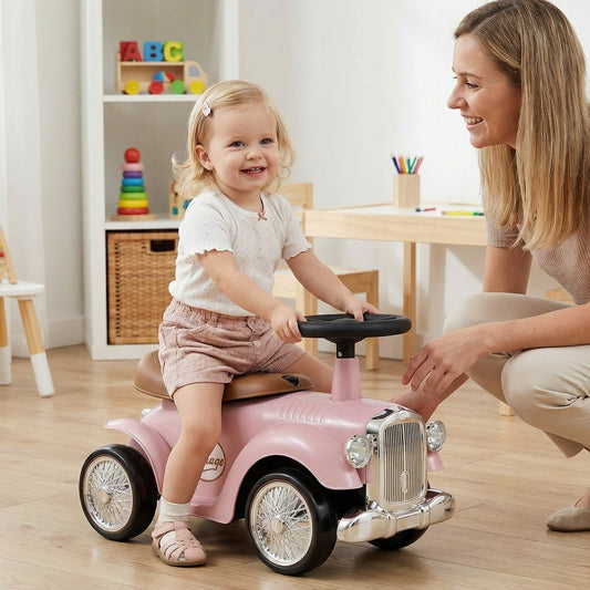 A smiling toddler sits on the pink push and pedal ride on toy with a woman beside her