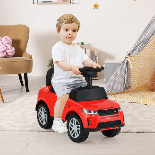 A toddler sits on the red ride on push car, steering it indoors