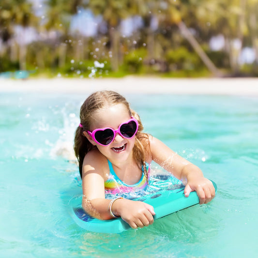 Young girl in pink heart sunglasses floating on a turquoise body board in the sea