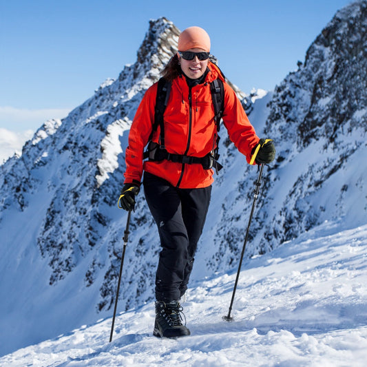 The yellow walking sticks are used by a woman hiking up a snowy mountain