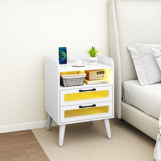 A white two-drawer nightstand with a charging station on top, shown next to a bed