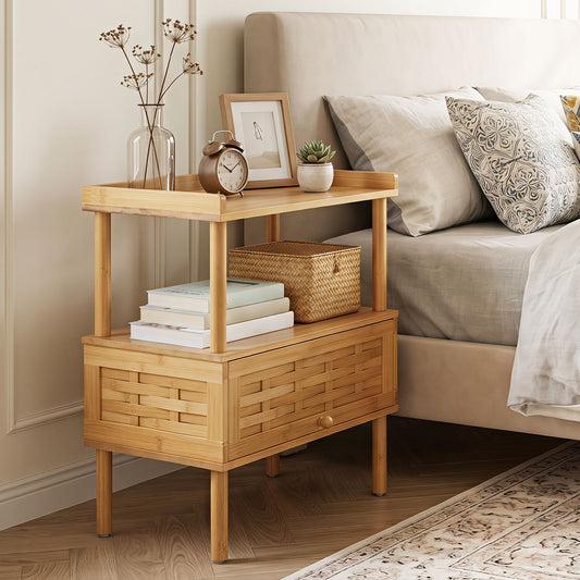The side table placed next to a bed with a vase, clock and books on its surface