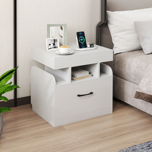 White bedside table with drawer and charging station on top, next to a bed