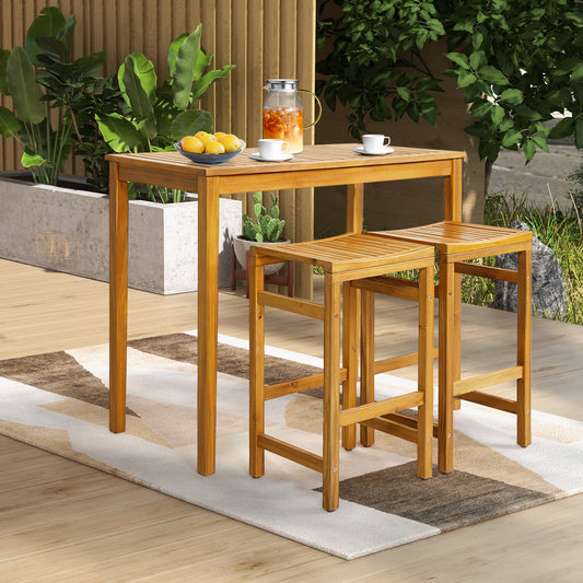 The acacia wood bar table is set up outside with two bar stools and plants