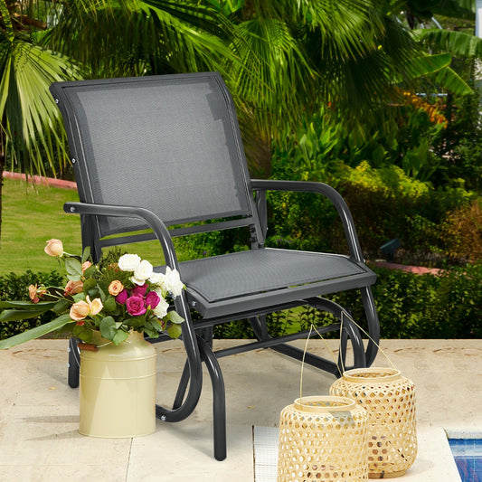 The grey outdoor single swing glider rocking chair for backyard is shown on a patio with flowers and lanterns