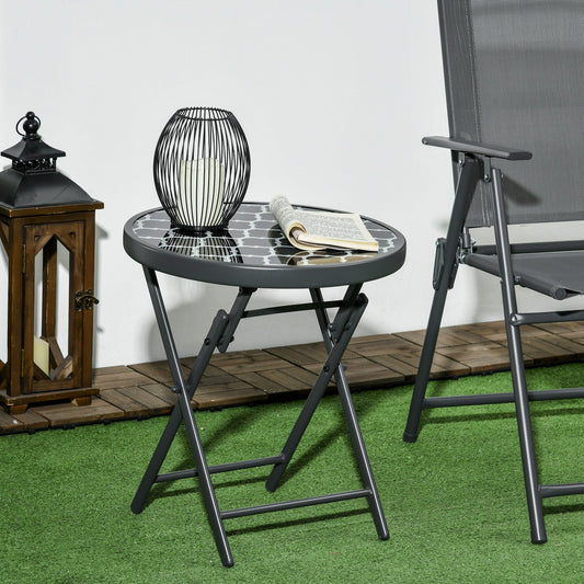 A round folding garden table with a black and white patterned glass top and grey metal legs, set on decking