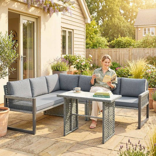 A woman sits on the grey rattan corner sofa set with a table on a patio