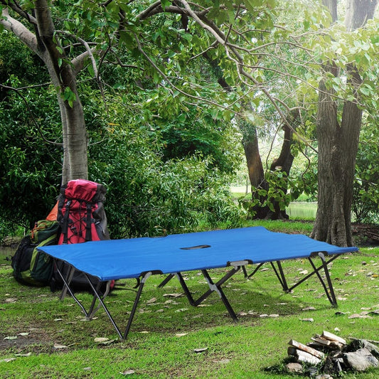 the blue camping bed set up in a woodland setting with backpacks and firewood nearby