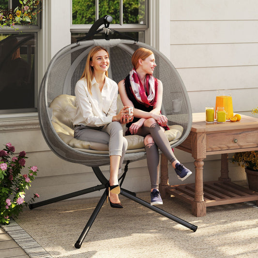 Two women sitting in the brown swing chair on a patio, enjoying drinks
