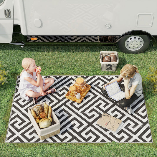 Two children having a picnic on the black and white geometric outdoor rug next to a campervan