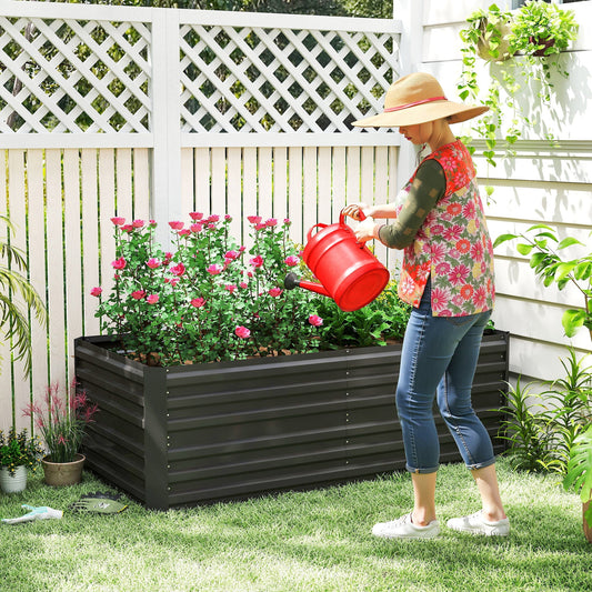 The garden planter filled with pink flowers being watered by a person in a garden setting