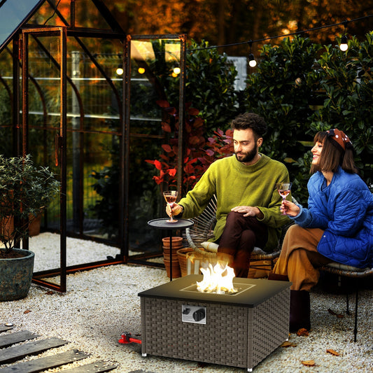 A couple enjoying drinks by the grey rattan gas fire pit table on a patio at dusk