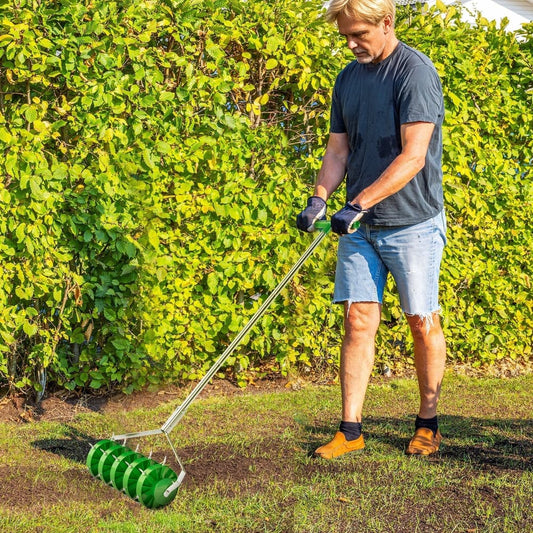 A man uses the manual grass spike roller to aerate his lawn on a sunny day