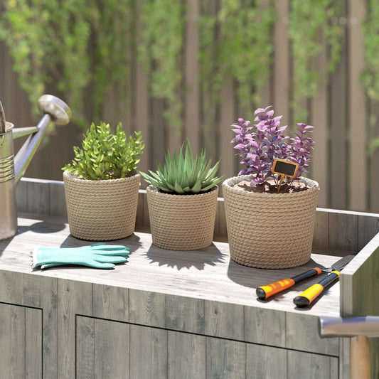 Three seagrass plant pots with plants on a wooden table with gardening tools