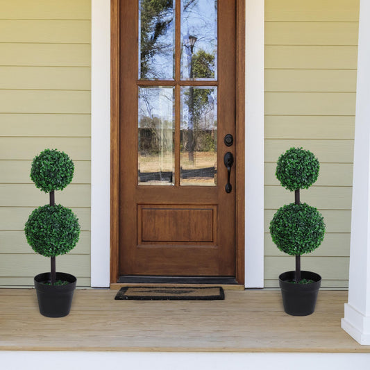 Two artificial boxwood ball topiary trees flanking a wooden front door on a porch