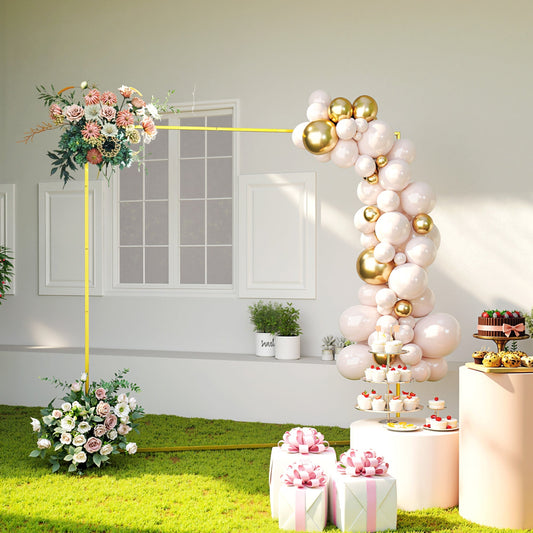 A gold wedding arch decorated with pink and white flowers and balloons, set up outdoors