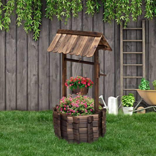 The wooden wishing well planter filled with pink and red flowers in a green garden setting