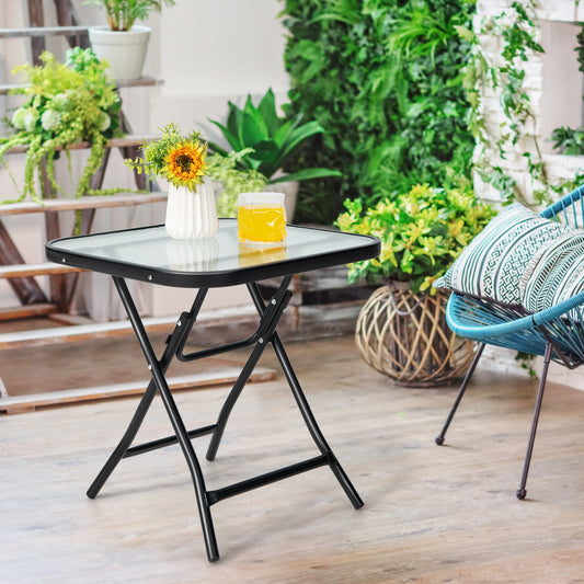 The patio table is set on a balcony with plants and a chair, showing its use as outdoor furniture