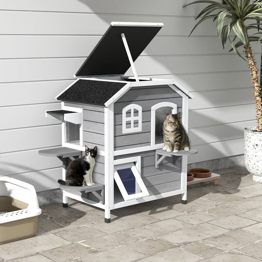 Two cats sitting on a grey wooden cat enclosure with an openable roof in an outdoor setting