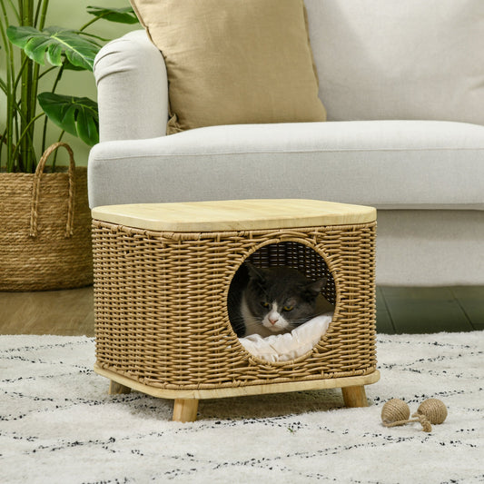 A grey and white cat sits inside the wicker cat house, which is placed on a rug next to a sofa