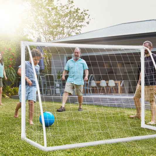 The soccer goal set up on a grassy lawn with a family playing a game together