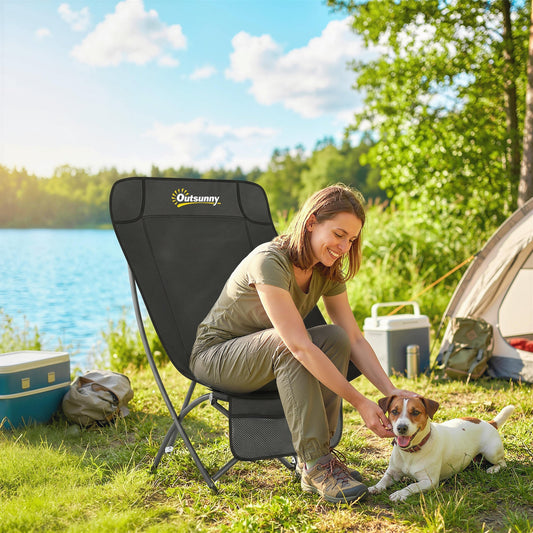 A woman and a dog sitting in a black folding camping chair next to a lake