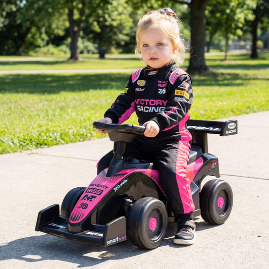 A young child in a racing suit sitting on the pink and black sliding car on a paved path