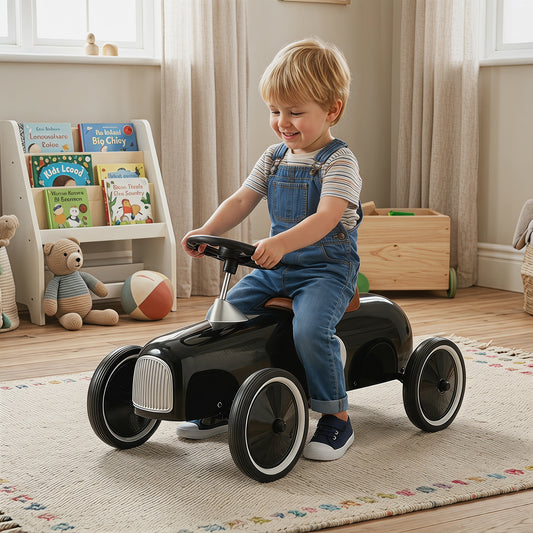 A happy toddler boy rides the black push and pedal ride on toy indoors on a rug