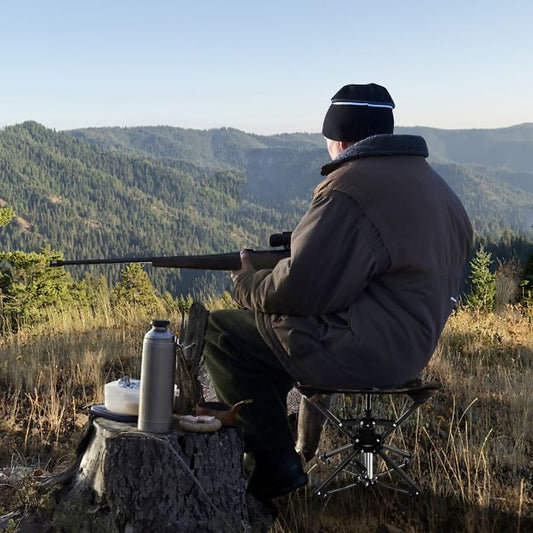Man sitting on a camouflage folding stool hunting in a woodland setting