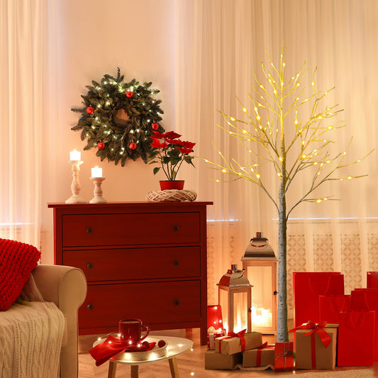 The Christmas tree is lit up and placed in a cosy living room next to a chest of drawers and a sofa