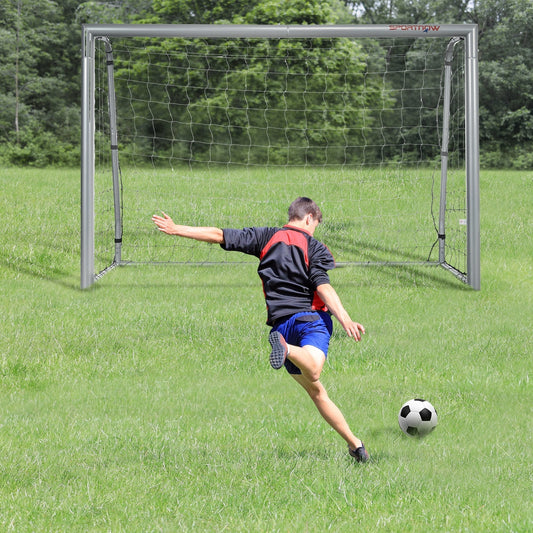The football goal set up on a grassy field with a person kicking a ball towards it