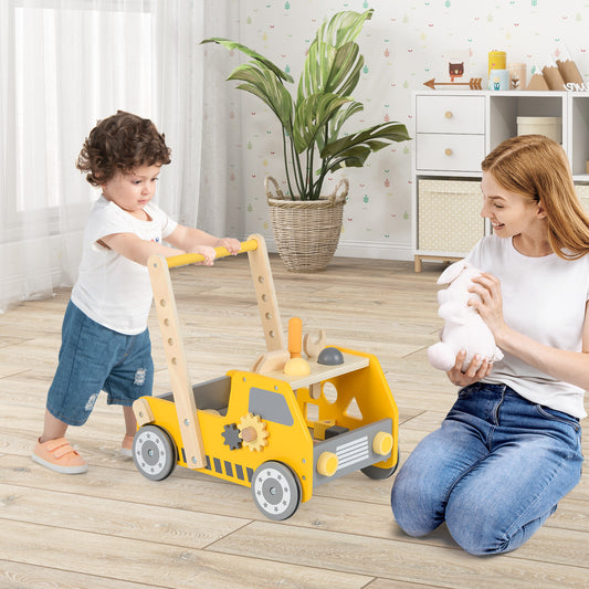 The baby walker being pushed by a toddler while a woman sits nearby holding a soft toy