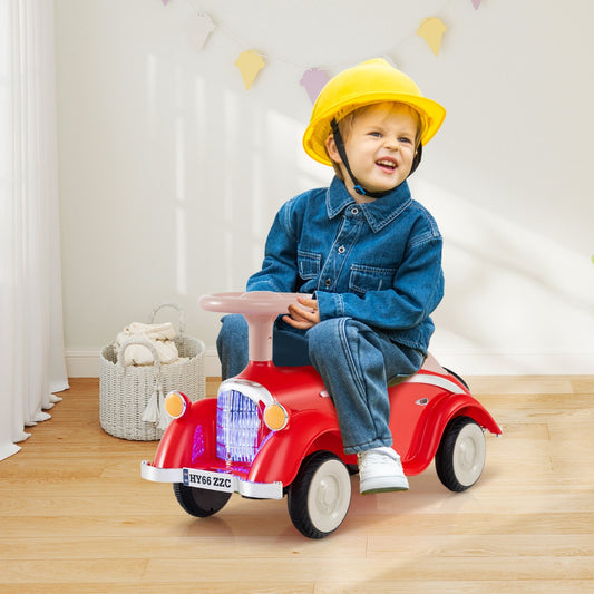 A red ride on car with a beige steering wheel being pushed by a child wearing a yellow hard hat