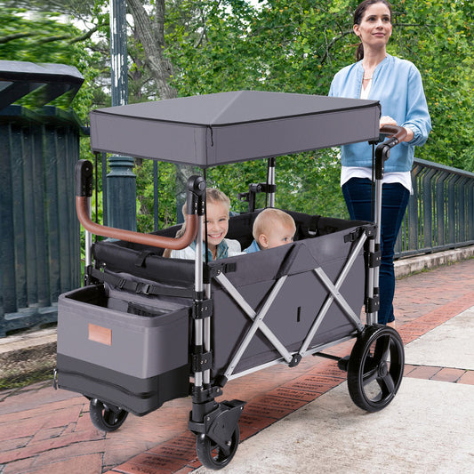 A woman pushes a grey double stroller wagon with two babies inside along a paved path