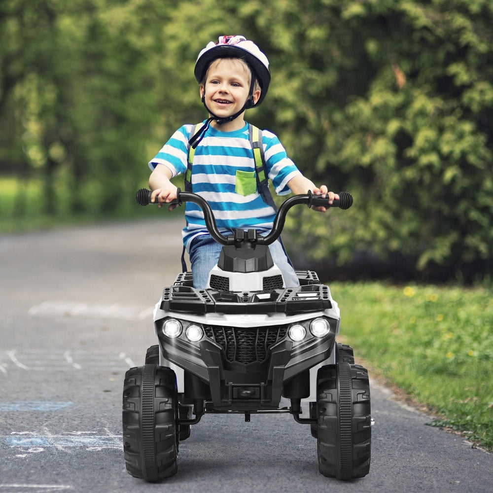A young boy rides the white kids electric quad bike down a paved path in a park