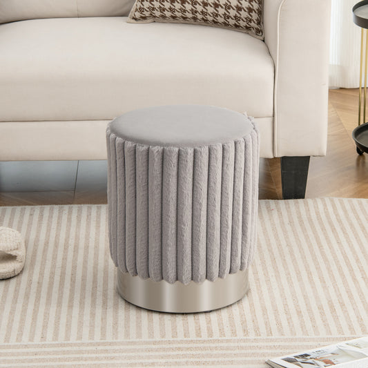 The grey ottoman with a smooth top and vertical tufted sides sitting on a rug