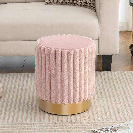 Pink upholstered footrest stool with a gold base placed on a rug next to a sofa