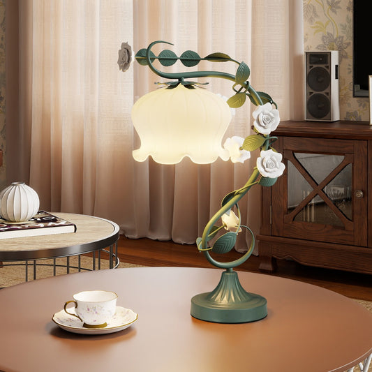 The floral table lamp with a glowing shade and green metal stem on a round table