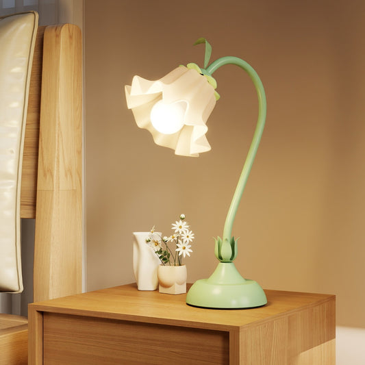 The green nightstand lamp sits on a wooden bedside table next to a vase of flowers