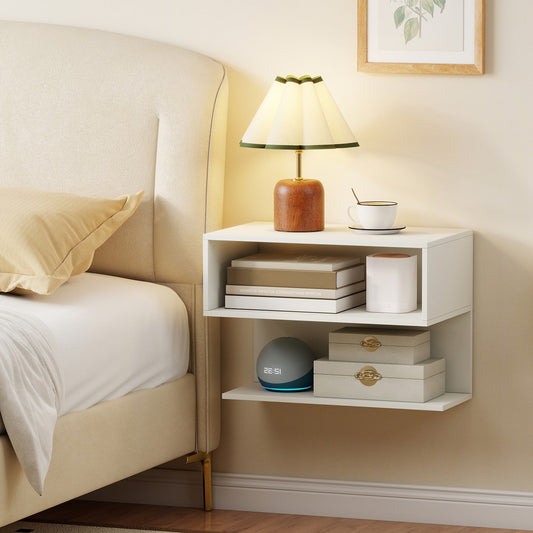 The white bedside table mounted on a wall next to a bed, with a lamp and books on top