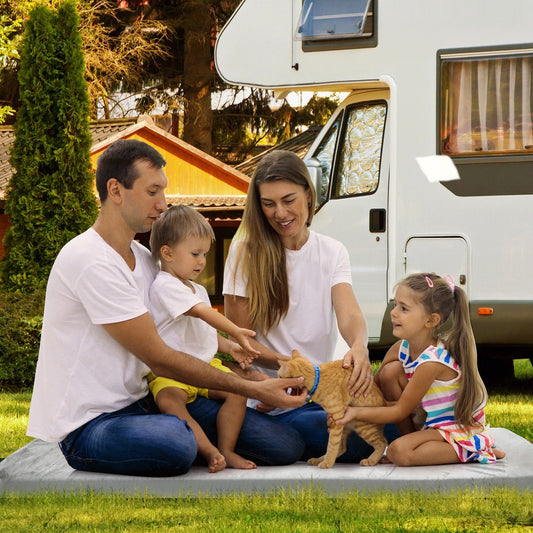A family with a cat sitting on the unrolled camping mattress outdoors next to a campervan